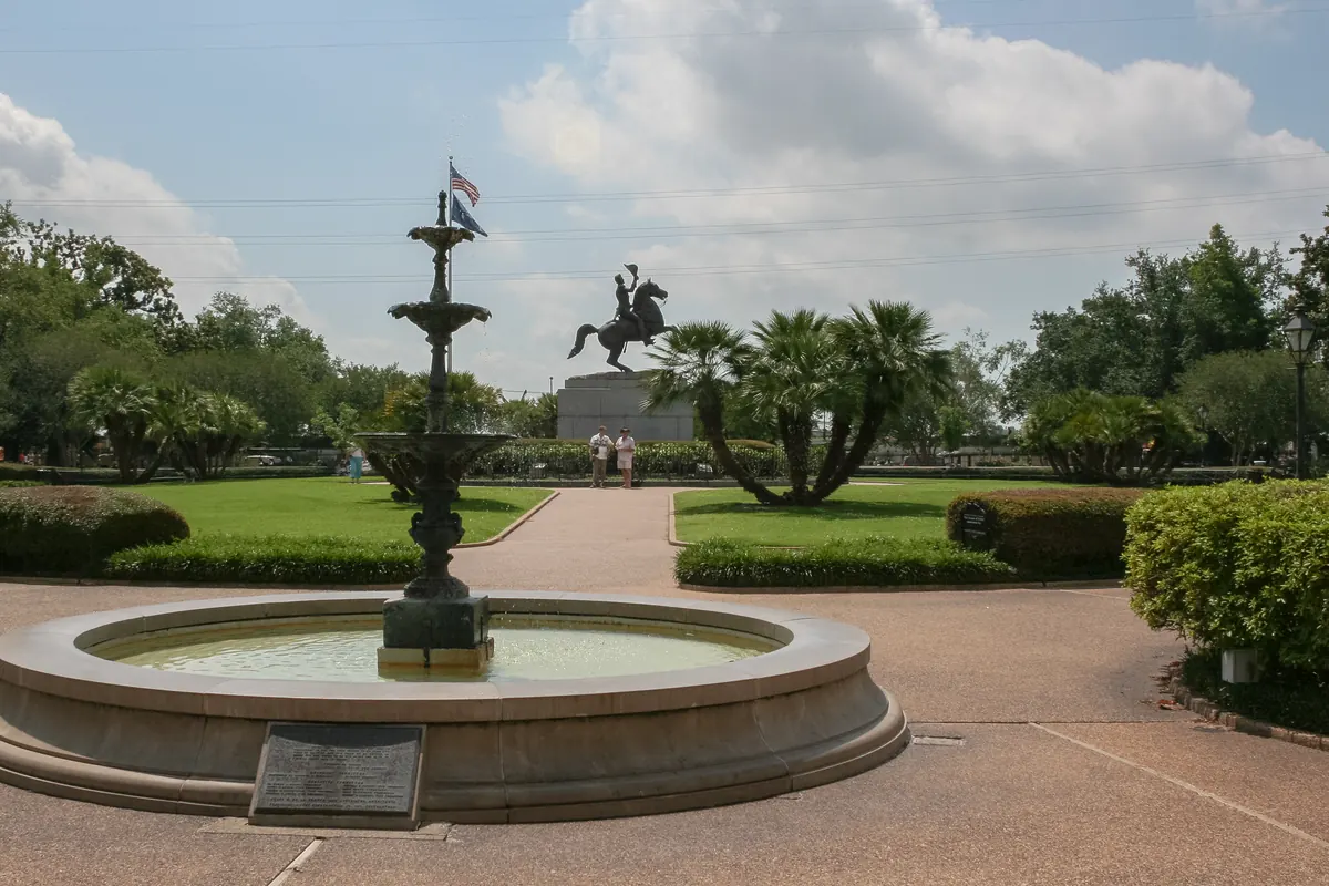The fountain and the statue of Andrew Jackson on horseback in Jackson Square, New Orleans, among palm trees and clipped hedges under a cloudy sky